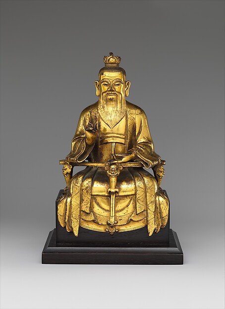 金色の衣をまとい、長いひげを垂らして座る道教の尊像。片手を胸の高さに上げる。
